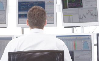 Overview photo: the back of a man in a white lab coat. In the background, six screens with data, charts and graphics.