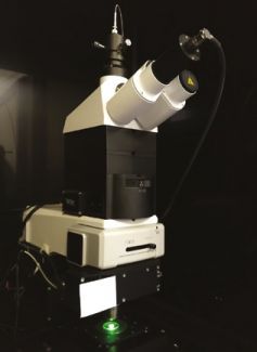 Overview photo. Modern white and black microscope against a black background.
