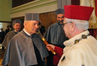 Prof. Stanisław Bielecki, TUL rector, in red gown and white ermine is resting a scepter on the shoulder of Prof. Andrzej Tylikowski in grey gown and is awarding him the DHC title of TUL.