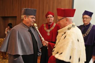Prof. Stanisław Bielecki, TUL rector, in red gown and white ermine is resting a scepter on the shoulder of Prof. Arieh Warshel in grey gown and is awarding him the DHC title of TUL. In the background, Prof. Piotr Paneth in red gown, vice-rector for science.