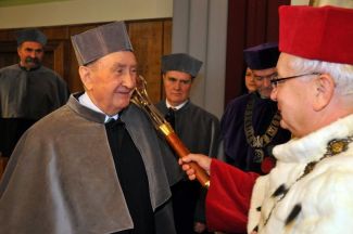 Prof. Stanisław Bielecki, TUL rector, in red gown and white ermine is resting a scepter on the shoulder of Prof. Eugeniusz Dembicki in grey gown and is awarding him the DHC title of TUL.