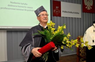Portrait photo: Prof. Jan Krysiński in grey gown with flowers and a red tube at the ceremony of awarding the DHC of TUL.