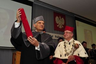 Prof. Jerzy Buzek in grey gown is holding a red tube with his arms up. Next to him, Prof. Stanisław Bielecki, TUL rector, in red gown and white ermine is holding a scepter.