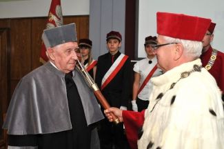 Prof. Stanisław Bielecki, TUL rector, in red gown and white ermine is resting a scepter on the shoulder of Prof. Leopold Jezierski in grey gown and is awarding him the DHC title of TUL. 