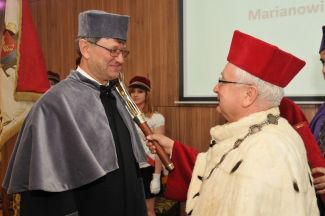 Prof. Stanisław Bielecki, TUL rector, in red gown and white ermine is resting a scepter on the shoulder of Prof. Marian Wiercigroch in grey gown and is awarding him the DHC title of TUL. 