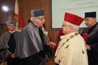 Prof. Stanisław Bielecki, TUL rector, in red gown and white ermine is resting a scepter on the shoulder of Vadim Anatolyevich Krysko in grey gown and is awarding him the DHC title of TUL.