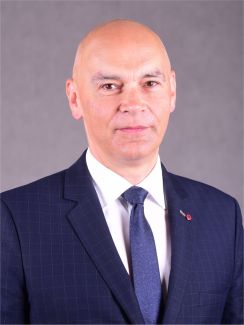Portrait photo: Prof. Witold Pawłowski, Assoc. Prof. Eng, in a blue jacket, white shirt and a tie against a grey background.