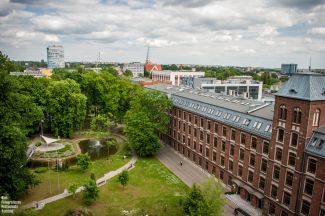 Kampus B z lotu ptaka: po lewej stronie zielone drzewa, po prawej stronie 4-kondygnacyjny, ceglany budynek Trzech Wydziałów.