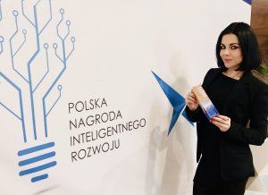 dr inż. Katarzyna Znajdek w ciemnym kostiumie przy ścianie z niebieską grafiką i napisem Polska Nagroda Inteligentnego Rozwoju.