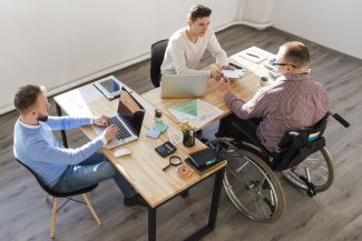Office, view from above: three men sit at a table, one of them in a wheelchair.