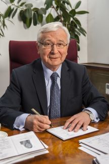 Portrait photo: Prof. Stanisław Bielecki is sitting at his desk and signing diplomas.