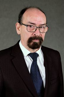 Zdjęcie portretowe: prof. Władysław Kamiński w ciemnym garniturze, białej koszuli i krawacie na szarym tle.