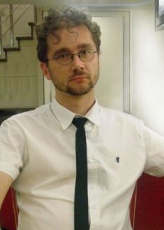 Zdjęcie portretowe: prof. Dawid Stawski w białej koszuli i czarnym, wąskim krawacie.