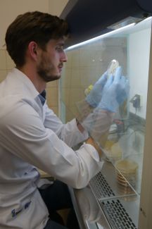 Dr. inż. Hubert Antolakiem w białych fartuchach i niebieskich rękawiczkach przy stanowisku laboratoryjnym.