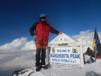 Prof. J. Banasiak w zimowym stroju alpinistycznym na szczycie Margherita Peak, najwyższym szczycie w Ugandzie przy białej tablicy informacyjnej.