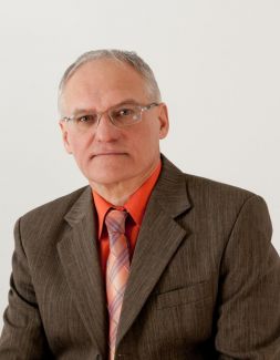 Portrait photograph: Professor Jan Avrejcevich in a grey suit, salmon shirt and tie against a pale wall.