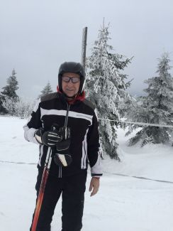 Prof. Piotr Kula w stroju narciarskim i z nartami. W tle zimowy pejzaż.