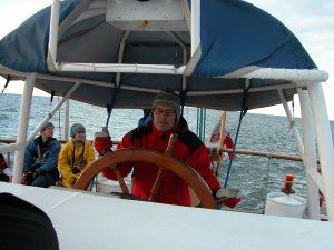 Pochmurny dzień: prof. I. Zbiciński w czerwonej kurtce stoi przy sterze łodzi. W tle morze.