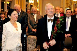 Prof. Jan Krysiński w smokingu trzyma różę, obok stoi małżonką z białej sukni (Haliną Krysińską). W tle goście.