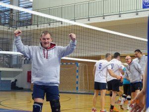 Prof. Krzysztof Jóźwik w podniesionymi rękoma w geście zwycięstwa. W tle boisko do siatkówki oraz drużyna.