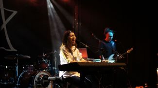 Eliza Tkacz na scenie, przy pianinie w trakcie koncertu. W tle gitarzysta.