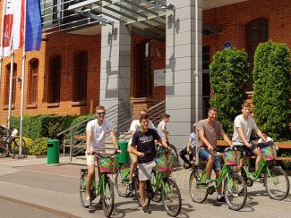 Studenci PŁ na rowerach przed ceglanym budynkiem IFE.