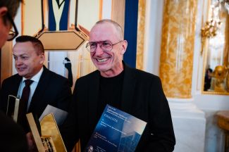 Prof. dr hab. inż. arch. Bartosz Hunger, uśmiechnięty, z dyplomem konkursu „Modernizacja Roku & Budowa XXI wieku” podczas gali na Zamku Królewskim w Warszawie.