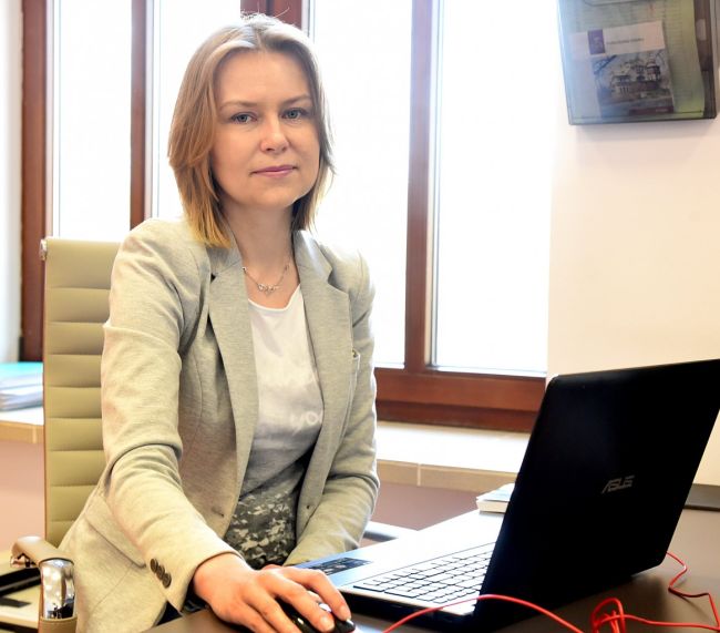 Zdjęcie portretowe: dr inż. Edyta Marcinkiewicz siedzi w gabinecie przy biurku i otwartym laptopie.