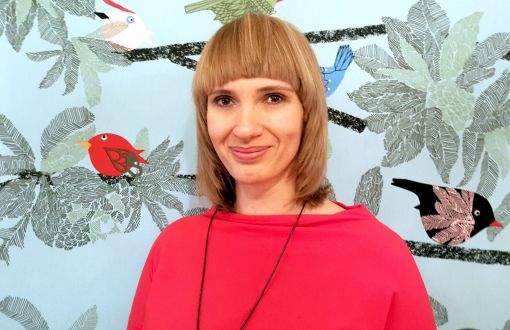 Zdjęcie portretowa: uśmiechnięta dr hab. Małgorzata Koszewska w czerwonej bluzce na tle abstrakcyjnej grafiki.