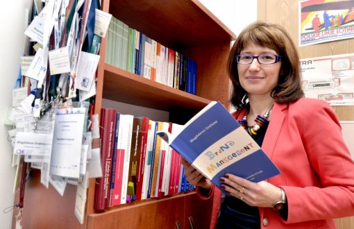 Portrait photo: Assoc. Prof. Eng. Magdalena Grębosz-Krawczyk, TUL Prof. is standing by a bookcase. She is holding one of the books open in her hands.