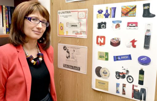 Portrait photo: smiling Assoc. Prof. Eng. Magdalena Grębosz-Krawczyk, TUL Prof. wearing a red jacket, is standing next to a cork board with colourful pictures.