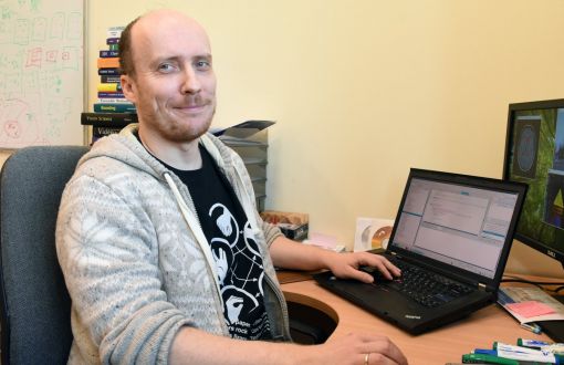 Zdjęcie portretowe: dr inż. Arkadiusz Tomczyk przy biurku, na którym stoi włączony laptop.