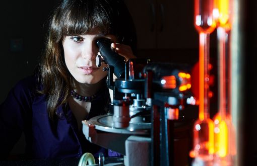 A woman facing front is looking through a microscope.