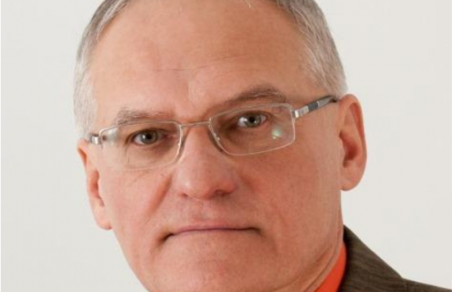 Zdjęcie portretowe: prof. Jan Awrejcewicz w brązowym garniturze i łososiowej koszuli na szarym tle.