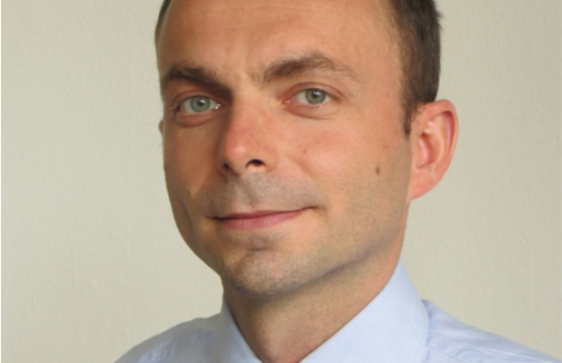 Portrait photo: Prof. Wojciech Pisula in a blue shirt and tie against a soft grey background.