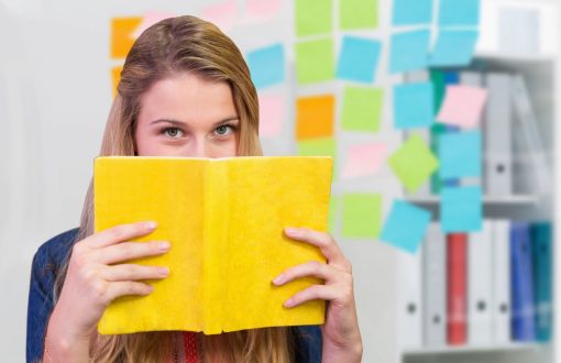 Overview photo: a girl hides behind a book with a yellow cover.