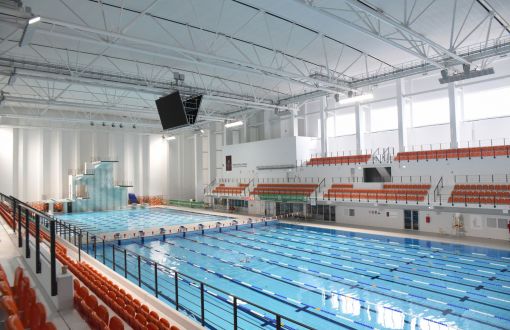 Baseny w Zatoce Sportu PŁ: 50-metrowy basen olimpijski oraz 25-metrowy. Widoczne trybuny z pomarańczowymi krzesełkami.