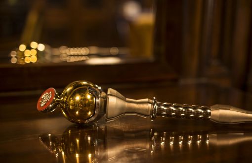 A silver TUL sceptre with gold elements lies on a tabletop in which a reflection can be seen.