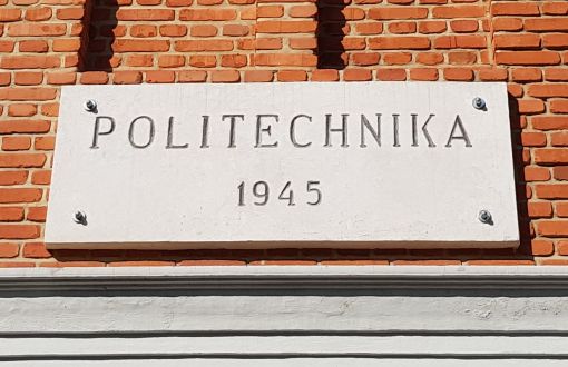 Szara tablica z napisem Politechnika 1945 przymocowana do ceglanego muru.