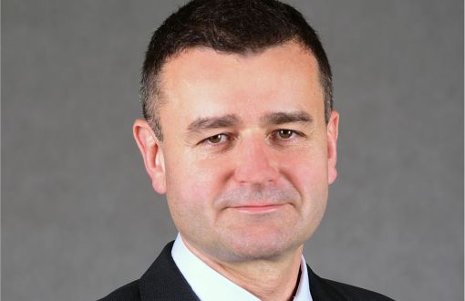 Zdjęcie portretowe: prof. Andrzej Romanowski w ciemnym garniturze, białej koszuli i niebieskim krawacie na szarym tle.
