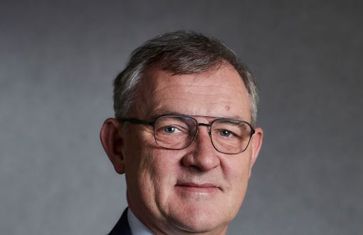 Portrait photo: Prof. Krzysztof Jóźwik in a navy blue suit, white shirt and a blue tie against grey background.