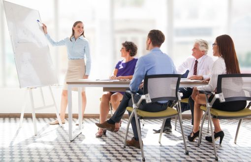 Spotkanie biznesowe: cztery osoby siedzą przy stole. kobieta stoi przy białej tablicy i coś prezentuje.