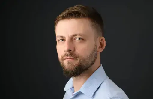 Zdjęcie portretowe dr Krzysztof Chyliński w niebieskiej koszuli na ciemnoszarym tle.