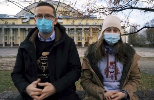 Mężczyzna (Adam Owczarek) i kobieta (Ola Bednarek) w bluzach z logiem PŁ i zimowych kurtkach siedzą na murku. W tle duży budynek - hala sportowa.