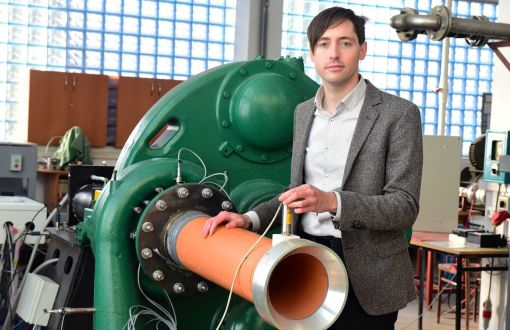 dr inż. Grzegorz Liśkiewicz w marynarce i białej koszuli pozuje do zdjęcia przy laboratoryjnej maszynie.