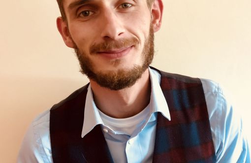 Zdjęcie portretowe: dr inż. Hubert Antolak w kraciastej kamizelce i niebieskiej koszuli na beżowym tle.