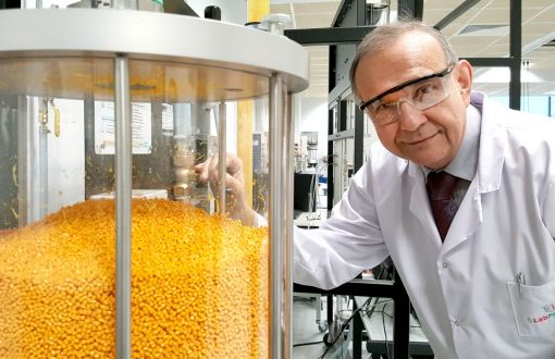 Portrait photo: Prof. Andrzej Górak, wearing a white lab coat and safety goggles, stands by a transparent container filled with yellow granules.