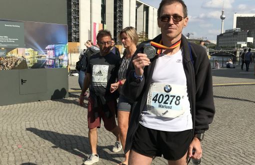 Prof. M. Wójcik stoi w stroju sportowym i prezentuje medal z maratonu w Berlinie z 2018 r.