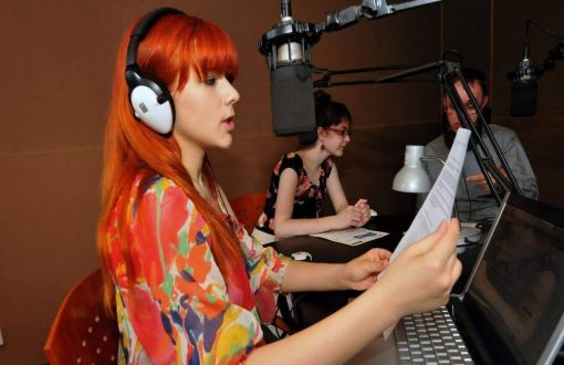 Rudowłosa dziewczyna w kolorowej sukience przed mikrofonem i komputerem w studiu Radia ŻAK