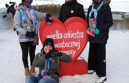 Czworo wolontariuszy WOŚP PŁ w zimowych stronach na śniegu trzyma duże, czerwone serce fundacji.